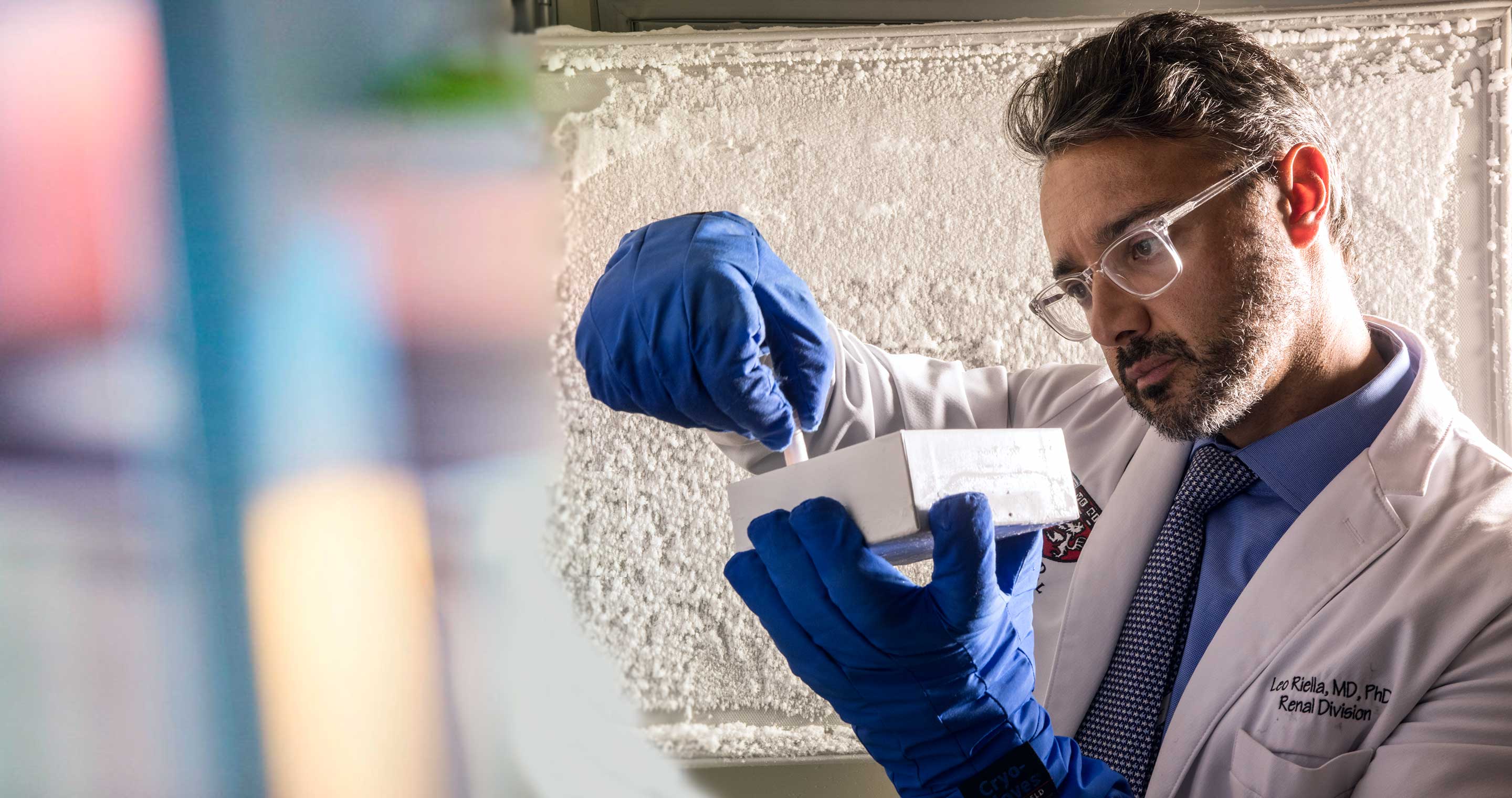 A doctor examines a vial that he lifts from a box.